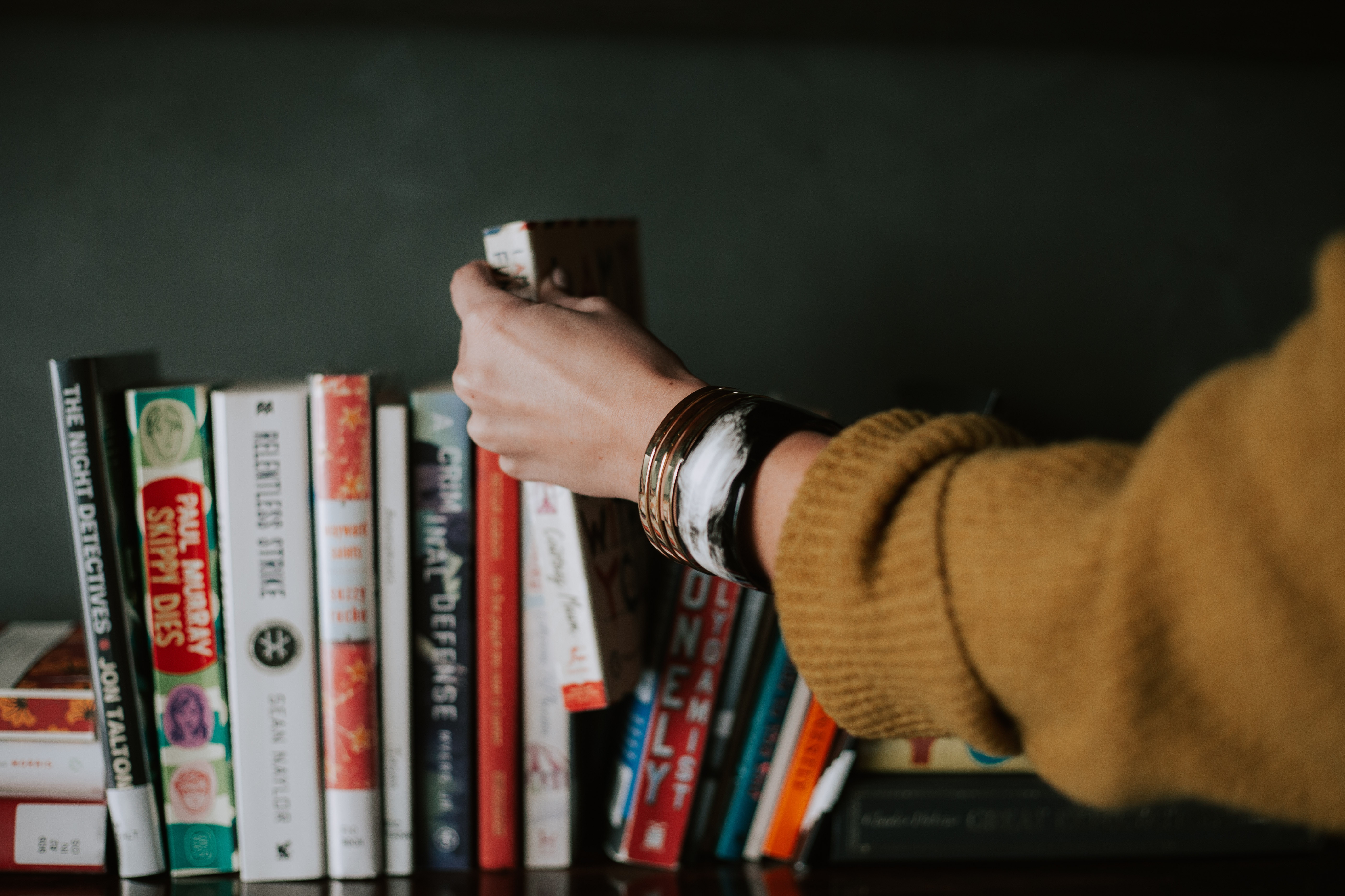Image of a book shelf, with someone taking a book out. Depicts the theme of the article, literary translation.