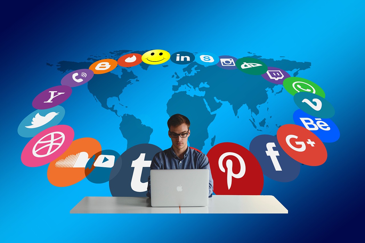 Man sitting at a laptop with social media logos behind him and map of the world.