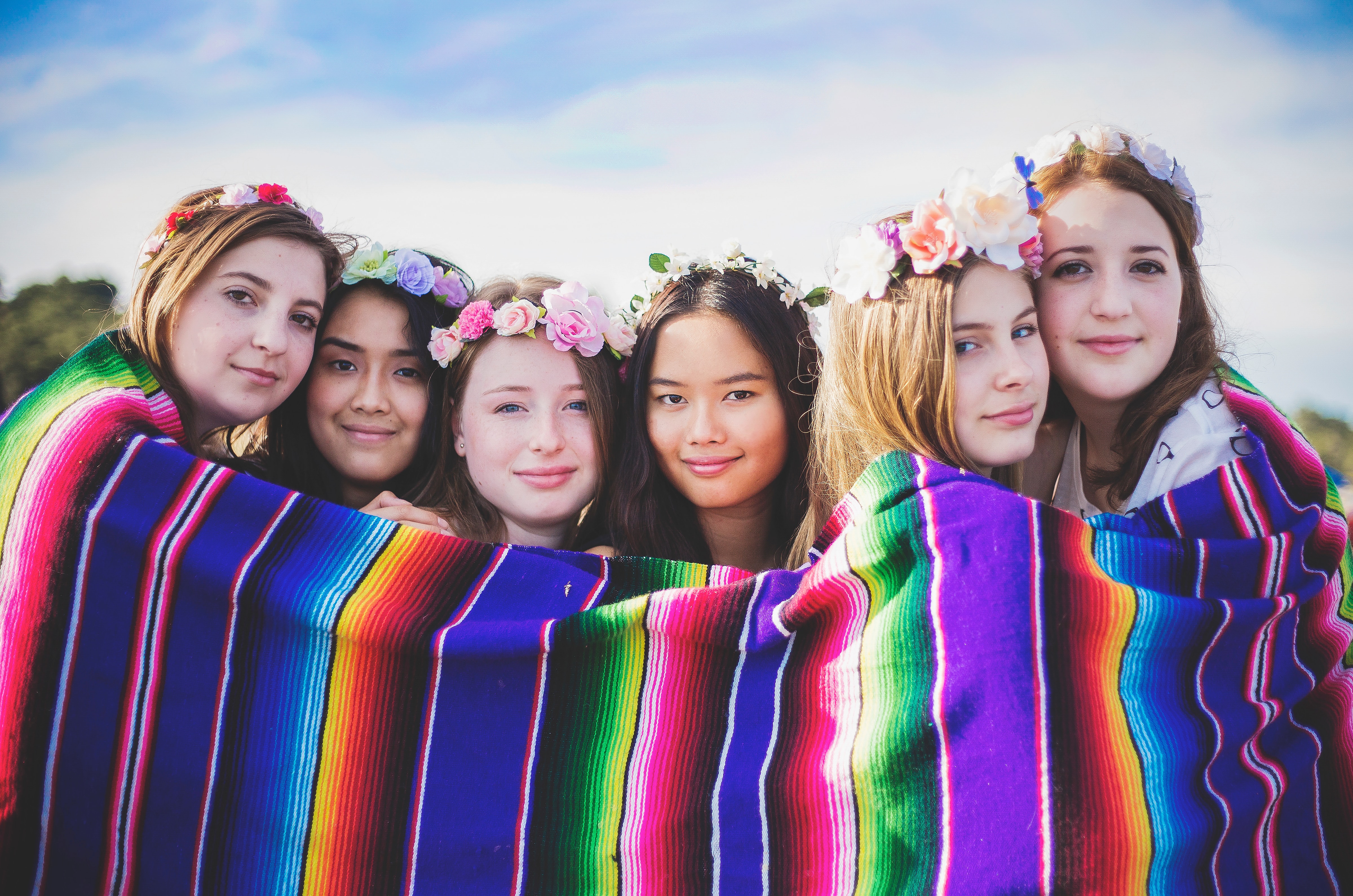 Image of six multinational female youths standing behind a multicoloured blanket