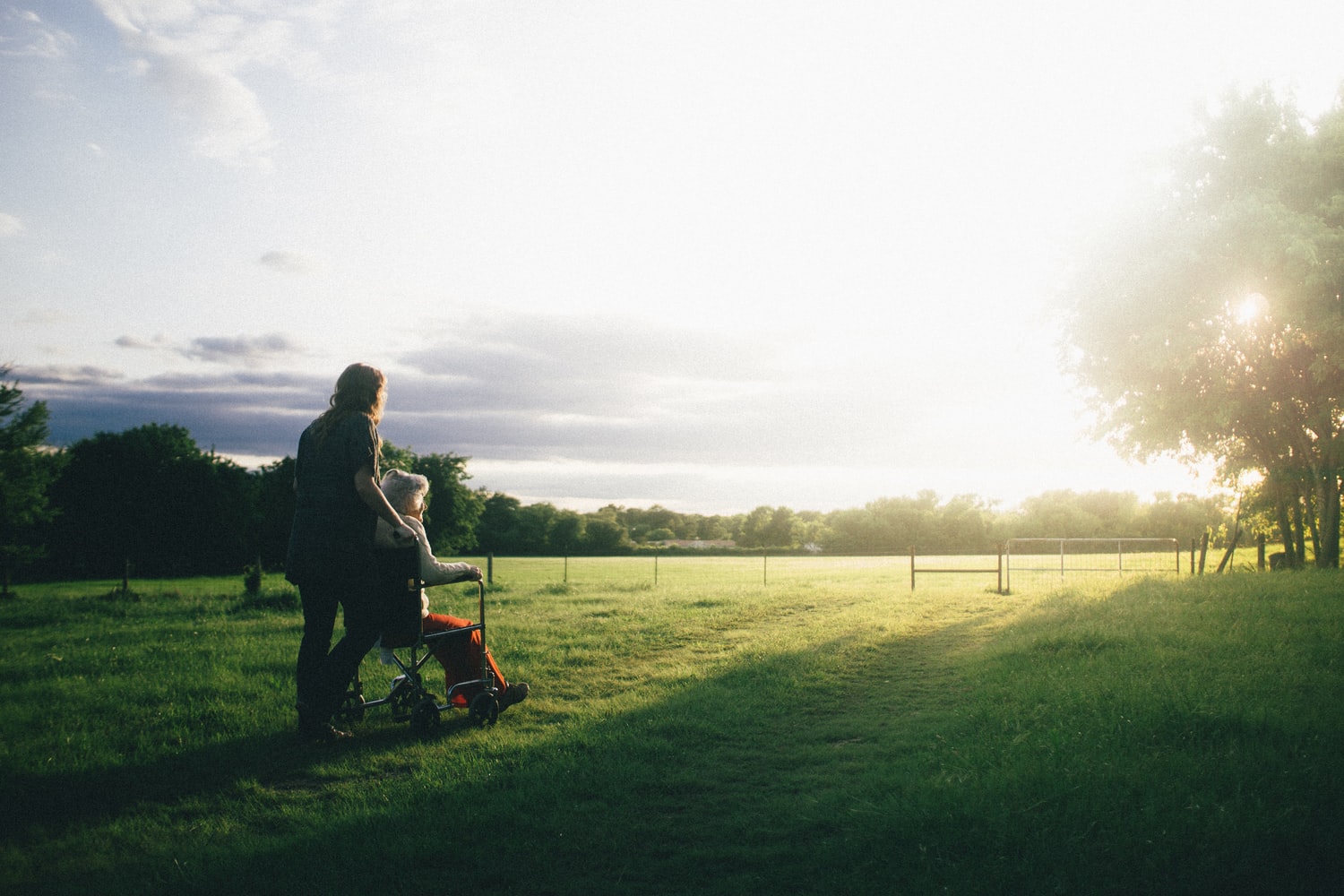 Lady pushing an older lady in a wheelchair through a meadow